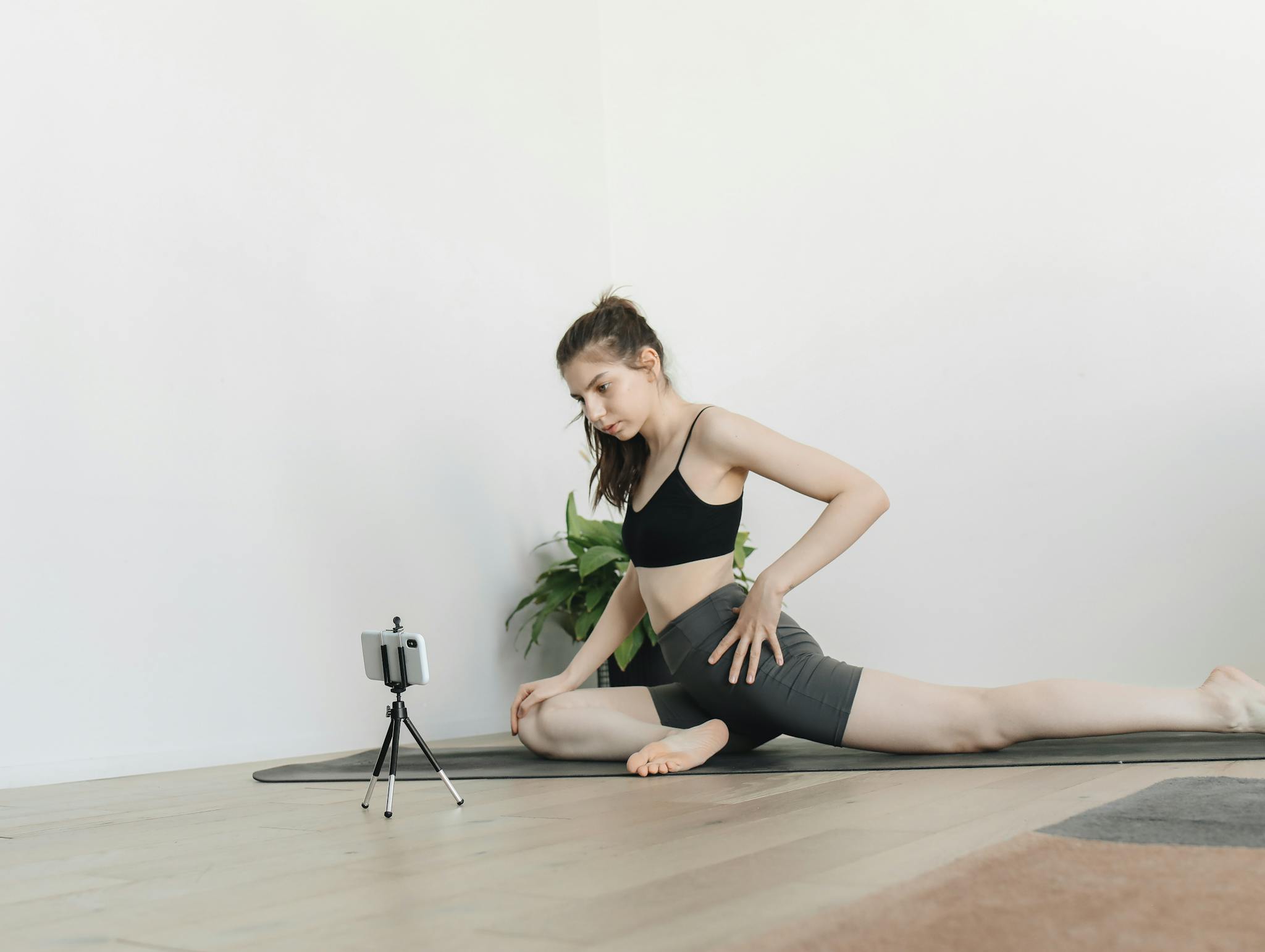 A young woman in active wear practicing yoga indoors with a camera setup for recording.